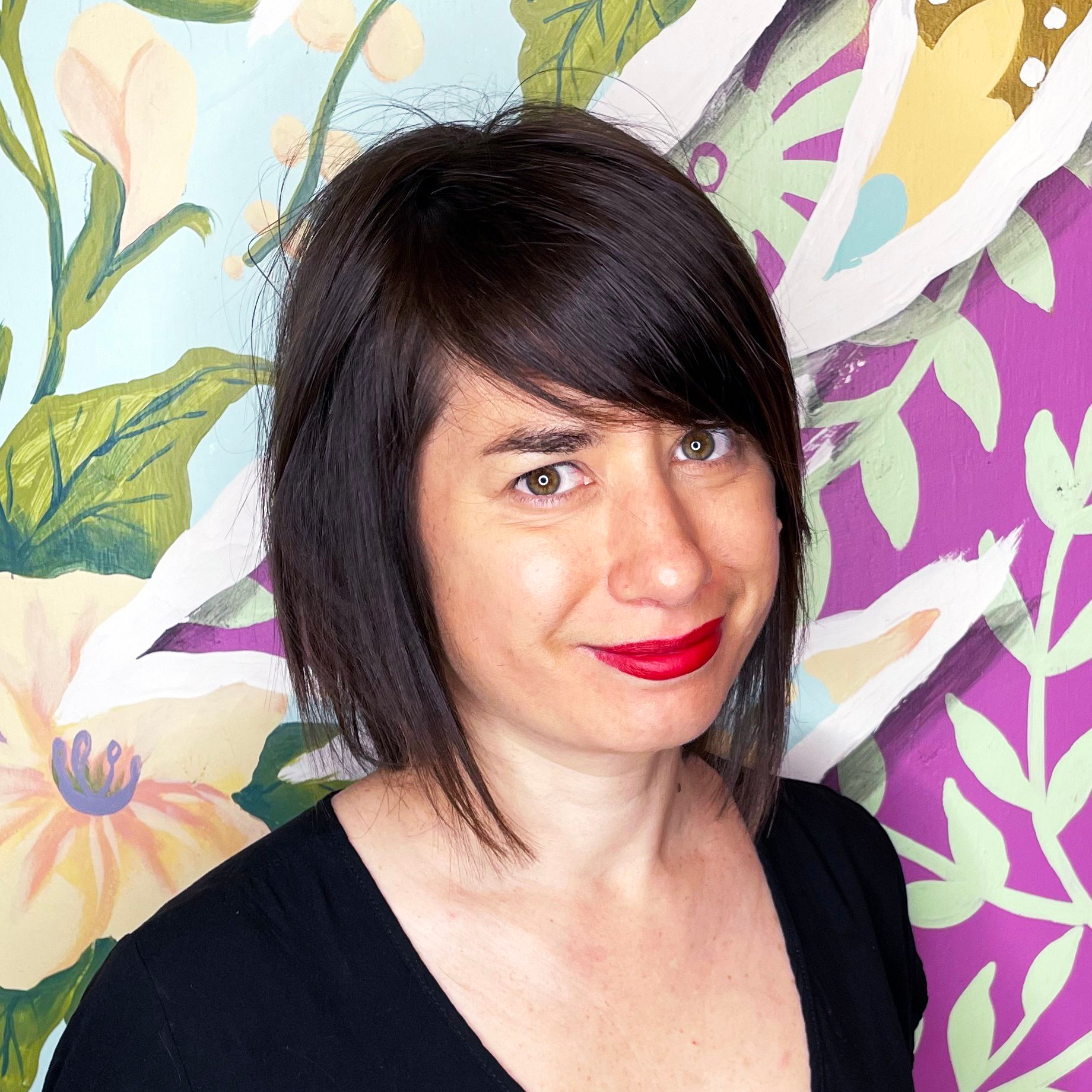 Portrait d'une femme souriante, yeux verts et cheveux noir au-dessus des épaules.