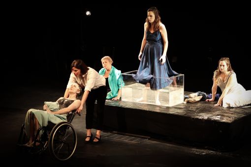 5 Maries, une les pieds dans le bassin, une autre sur un fauteuil roulant, une qui la tire, deux sont assises sur scène.